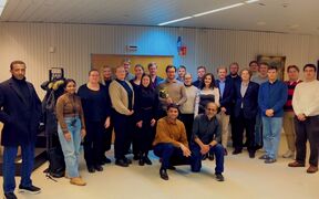 Group of adults indoors posing for a photo; one holds a trophy, two crouch in front, faces blurred