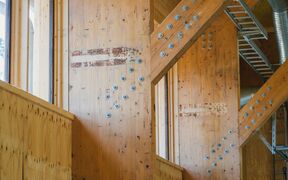 Interior with light timber beams and metal bolts, showing a wooden structure with exposed ducts and ladder.