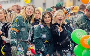 Studenter i gröna overaller på ett livligt utomhusevenemang, ballonger och en gör fredstecken