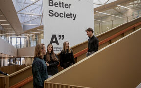 Four students talking on an indoor staircase beside a large white Business Better Society sign