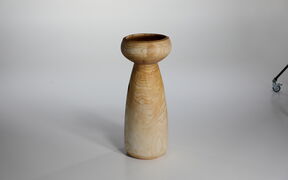 Tall, light brown wooden pedestal or vase with rounded top, standing on a plain light background