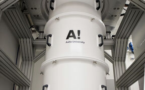 Large white cylindrical lab device in a metal frame, labelled Aalto University