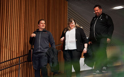 Kolme ihmistä kävelee vierekkäin alas portaita.