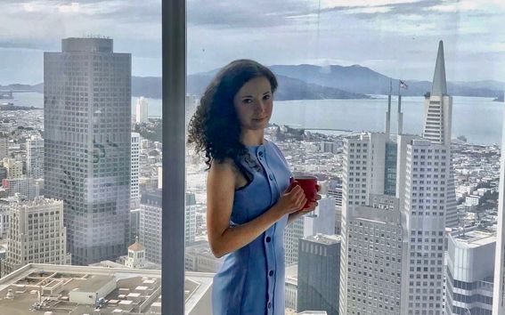 Elonora Nazander standing by a window overlooking a city view.