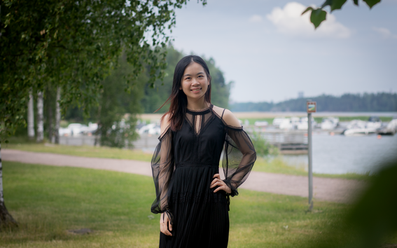 Female student standing outdoors in a park, harbour and trees in the background