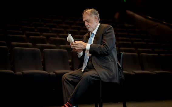 Tumma-asuinen mies istuu elokuvateatterikatsomon edustalla ja ottaa maskia pois kasvoiltaan, katse maskissa.