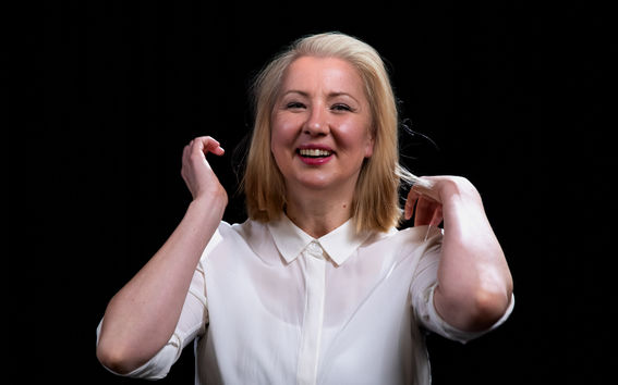 Toimittaja Katrina Jurvan hymyilevät kasvot on käsitelty kuvaan nykyistä vanhemmiksi. Hän on pukeutunut valkoiseen paitaan, kuvan tausta on musta.