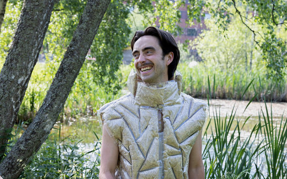 Hymyilevä mies, jolla on päällä topattu liivi, seisoo osmankäämilammen edessä.