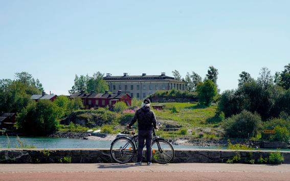 A man photographed from behind, standing with his bike looking at an older house building.