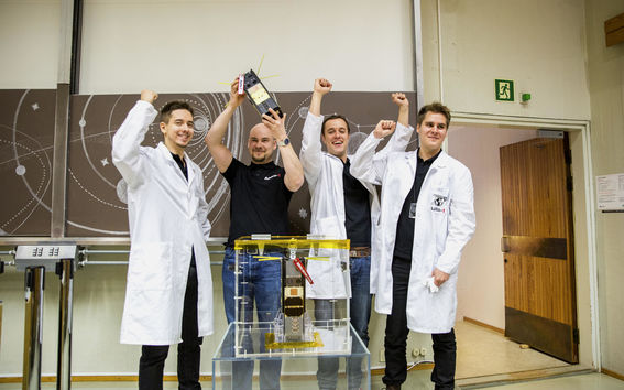 Neljä ihmistä esittelee iloisena satelliittia.