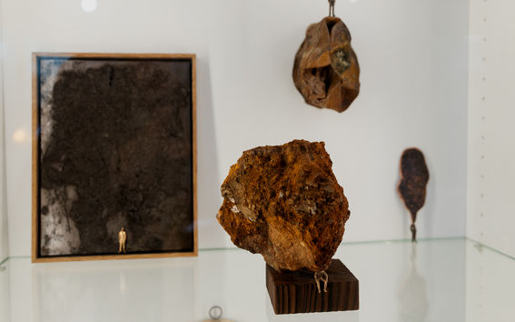 Four miniature figures in different parts of a display around rocks and dark shapes. One figure stands on a framed dark surface.