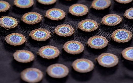 Close-up of round, embroidered patches with blue centres and brown edges, arranged in rows on a dark fabric.