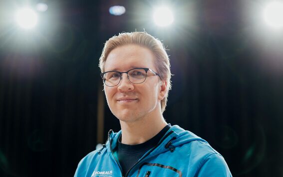 Henkilö sinisessä takissa kirkkaiden valojen alla, musta tausta.