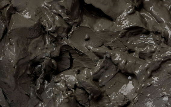 A close-up of wet, grey clay with a shiny, smooth surface texture and multiple grooves.