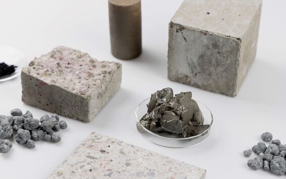 Various concrete samples and materials, including a cylinder, cubes, pebbles, and a dish with grey clay.