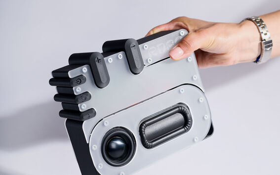 A hand holding a grey and black gadget resembling a retro camera against a white background.