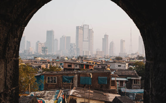 Näkymä kaariportin läpi kaupunkimaisemaan, taustalla moderneja pilvenpiirtäjiä ja etualalla vanhoja rakennuksia.