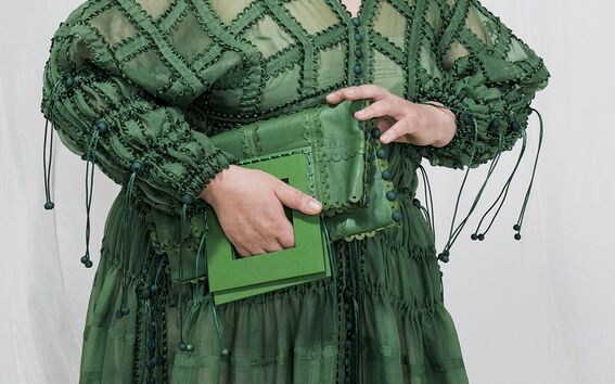 Person wearing a green dress with intricate patterns, holding a matching green clutch bag.
