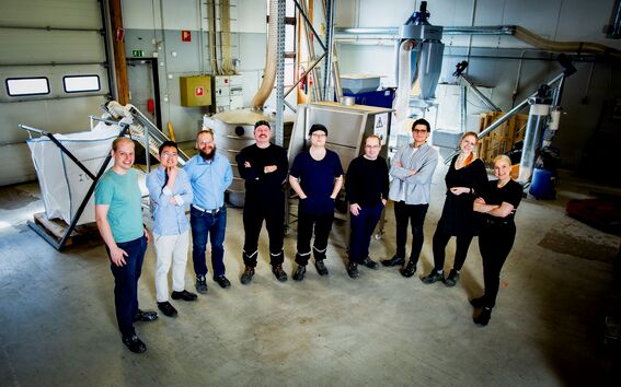 A group of people standing in an industrial workshop with machinery and equipment in the background.
