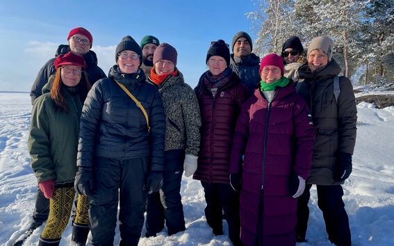 A group of people in winter clothing standing on snow with trees in the background.