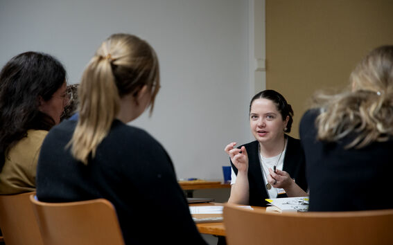 Group of people seated around a table in a meeting, one person speaking with gestures