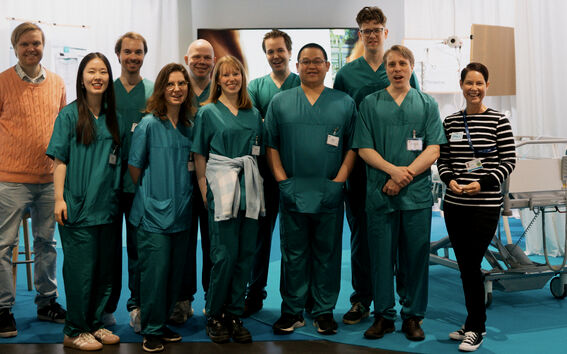 Group of people in green medical scrubs and casual clothes standing indoors near hospital equipment