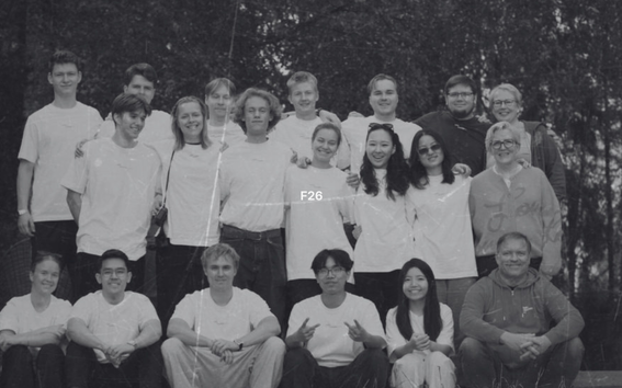 Large group of young adults in light shirts pose outdoors together, smiling in three rows