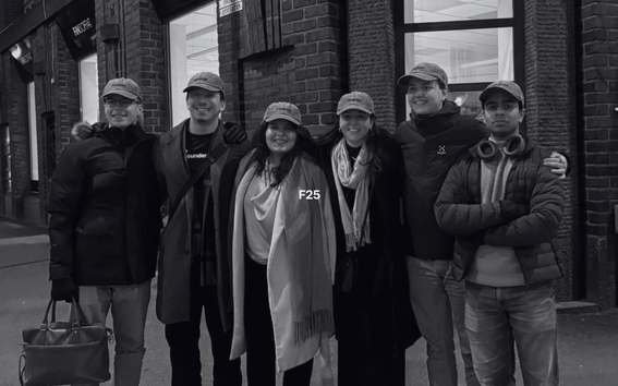 Six people in caps pose arm in arm on a city street at night by a brick building