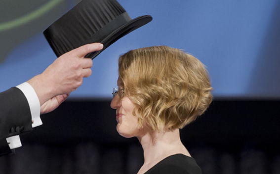 Tohtoriksi valmistunut nainen vastaanottamassa päähänsä mustaa tohtorinhattua promootiossa.