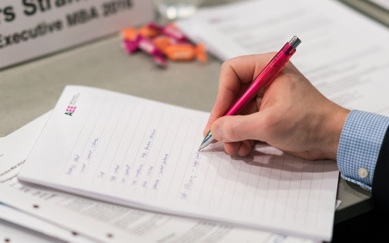 Close up on a hand writing on a note pad with the Aalto EE logo