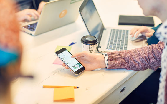 Close-up on student searching information on their mobile phone at a table with laptops