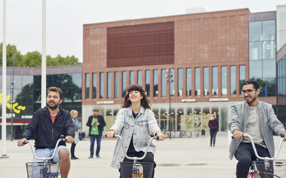 Thre students bicycling in front of the Väre building.