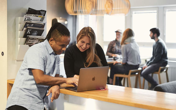 Opiskelijat nojaavat pöytään ja katsovat jotain kannettavalta tietokoneelta