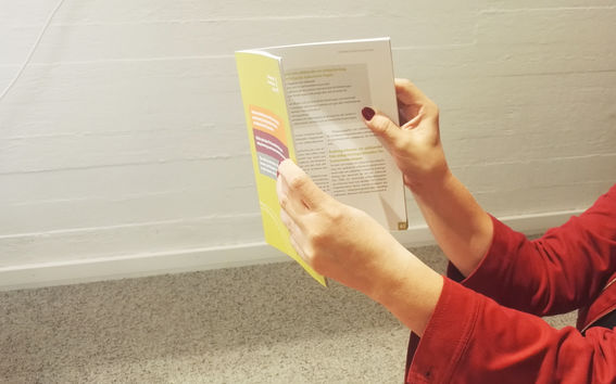 Nainen lukee opasta. Kuvassa näkyy lisäksi henkilön kädet ja punaiset hihat.