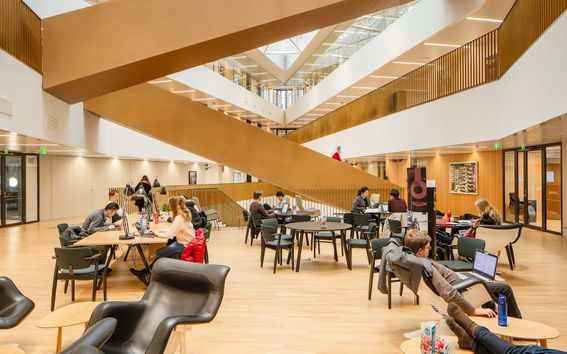 People studying in the School of Business main building with a large staircase in the background.