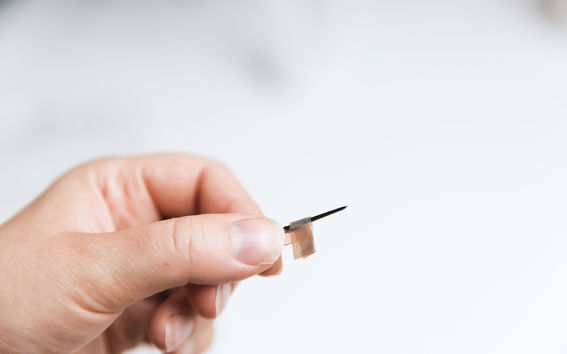 Käsi pitelee neula-tyyppistä anturia, joka soveltuu esimerkiksi mittauksiin aivoleikkeissä. Anturin kärjen halkaisija on vain yhden mikrometrin suuruinen. Kuvaaja: Iiro Immonen.