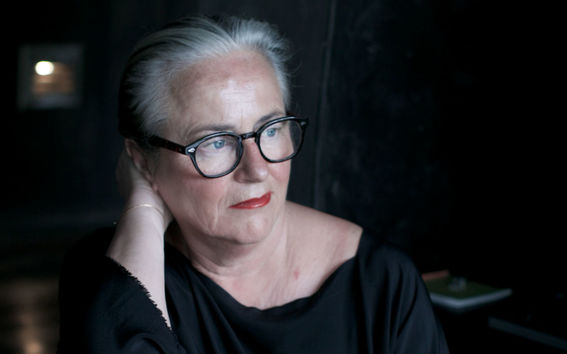 Nainen katsoo tummasävyisessä kuvassa oikeaan alaviistoon käsi pään takana