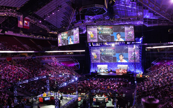 Large arena filled with a crowd watching a game of DOTA2 projected on big screens