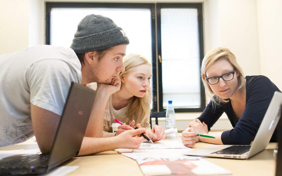 A group of three students engaging in teamwork, one presenting something from her laptop's screen