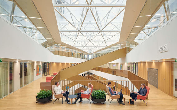 Students sitting in a light-colored building, face-to-face with laptops in colourful chairs
