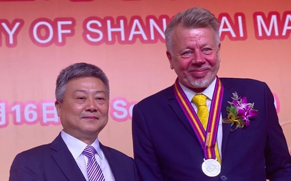 kuvassa kaksi miestä, joista toinen esittelee mitali kaulassa saamaansa kunniakirjaa punaisissa kansissa