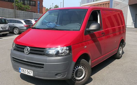 A red Volkswagen van is parked in a parking lot, with other cars and buildings in the background.