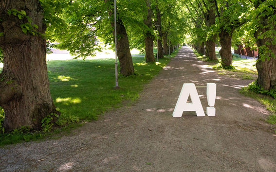 Yliopiston 3D-tulostettu logo hiekkatiellä kampuksella.