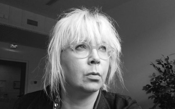 Vaaleahiuksinen nainen tummissa vaatteissa katsoo mustavalkokuvassa yläviistoon totinen ilme kasvoillaan