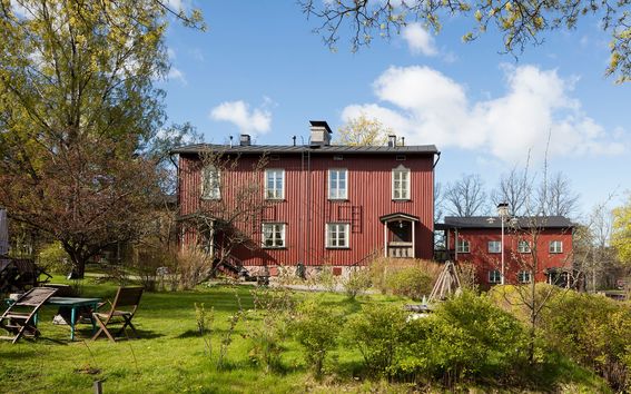 Kesäinen pihanäkymä: istuinryhmä nurmikolla punaisten puutalojen edustalla