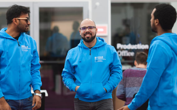 Henkilökuvassa hymyilevä, parrakas ja silmälasipäinen Bruno Duarte on kahden muun miehen kanssa. Heillä kaikilla on siniset SECCLO-tunnuksin varustetut hupparit päällään.