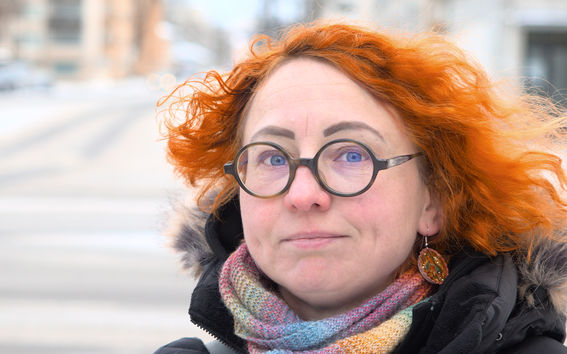 Punatukkainen silmälasipäinen nainen katsoo kameraan musta takki ja värikäs kaulaliina yllään.