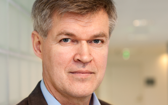 Photo of Tapani Vuorinen in a brown blazer looking straight into the camera.