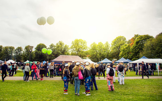 Students in student overalls and graduation caps on Otaniemi campus with festival-like tents and market stands on a summer's day