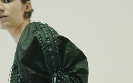 Sivuprofiili mallista vihreässä, koristeellisessa mekossa.